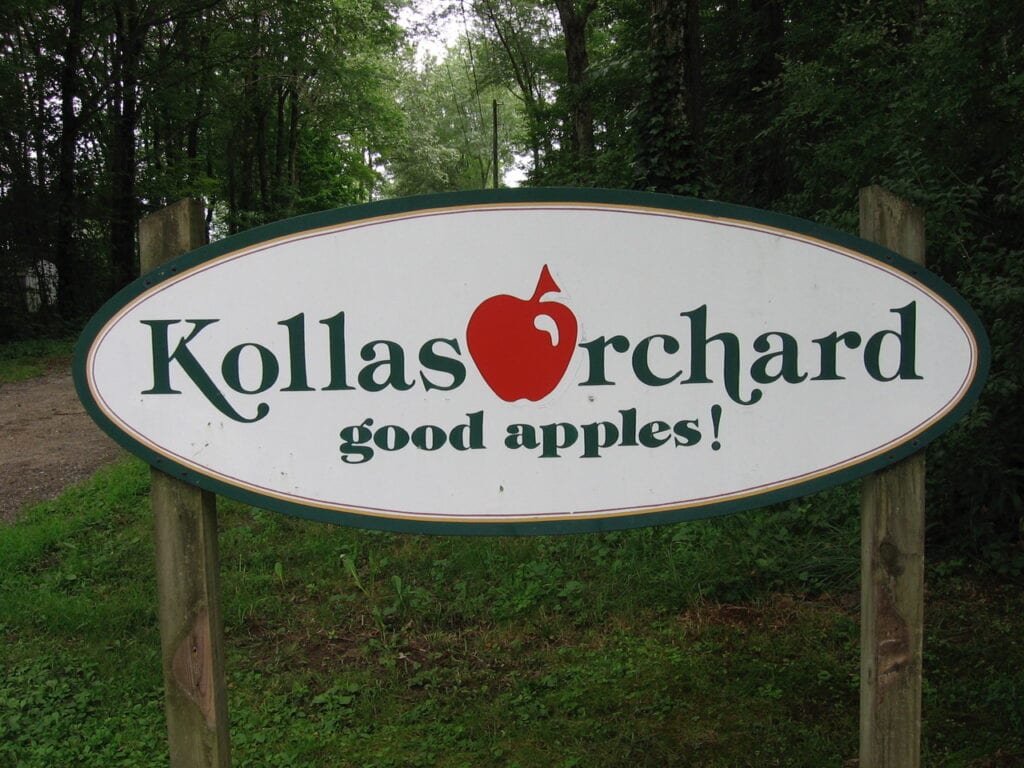 Sign for Kollas Orchard with an apple logo and slogan.